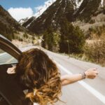 woman riding on vehicle putting her head and right arm outside the window while travelling the road